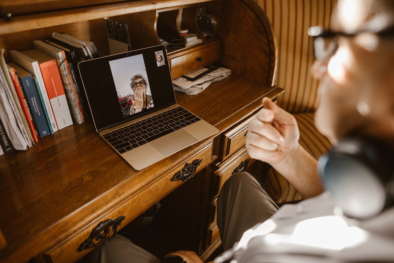 Adult video calling on a laptop at a wooden desk, capturing a long-distance relationship moment.